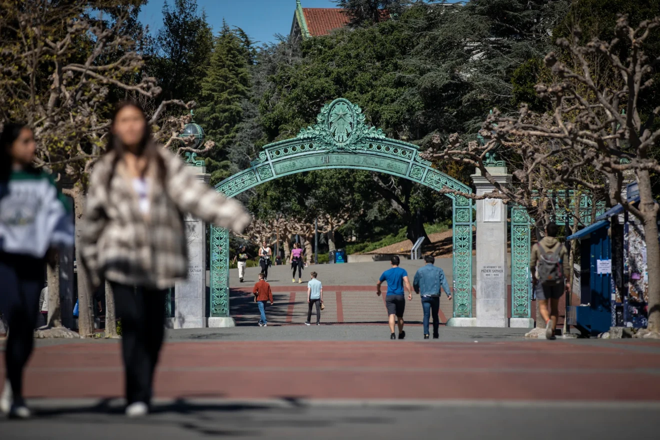Two students walk in the foreground as a large, decorative metal gate is shown on the UC Berkeley campus.